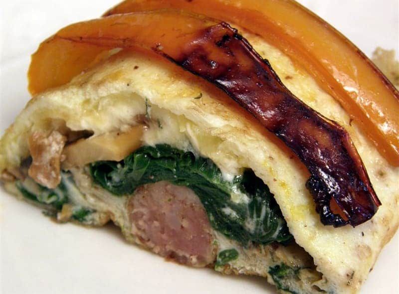 A close up of a sandwich with spinach and bacon on a white plate