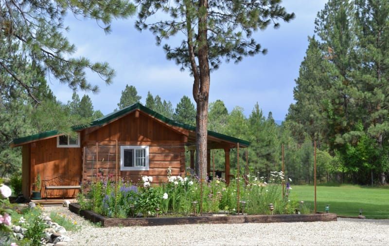 A small log cabin is surrounded by trees and flowers.
