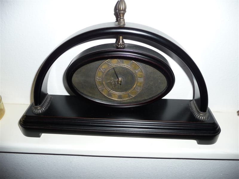 A black clock with roman numerals sits on a shelf