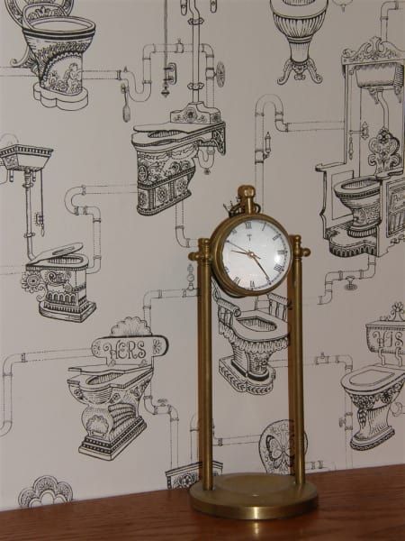 A clock on a table in front of a wall with drawings of toilets