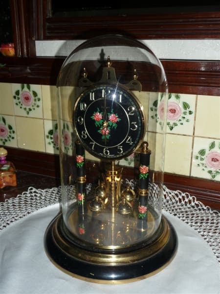 A black and gold clock with flowers on the face is under a glass dome