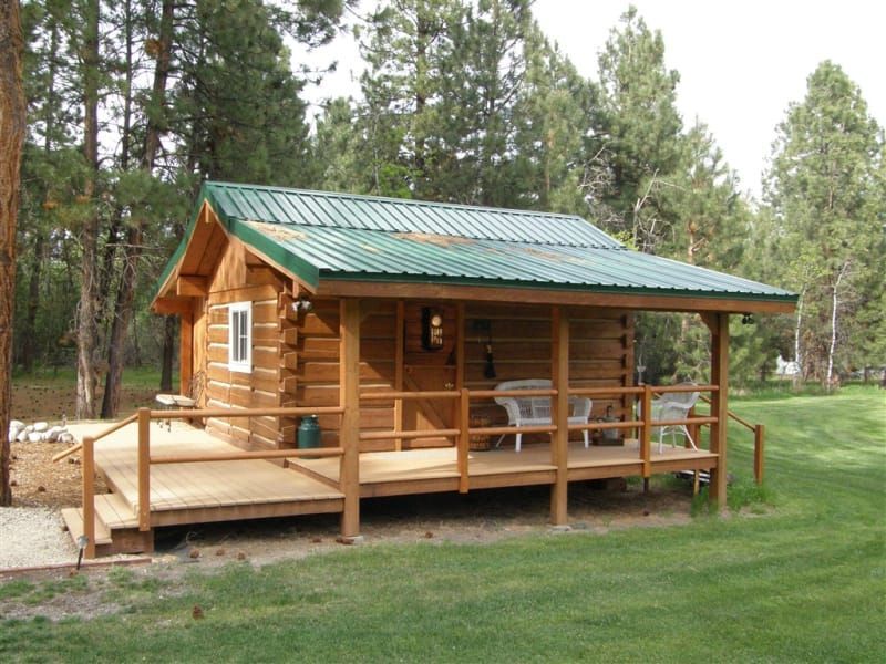 A small log cabin with a green roof and a porch