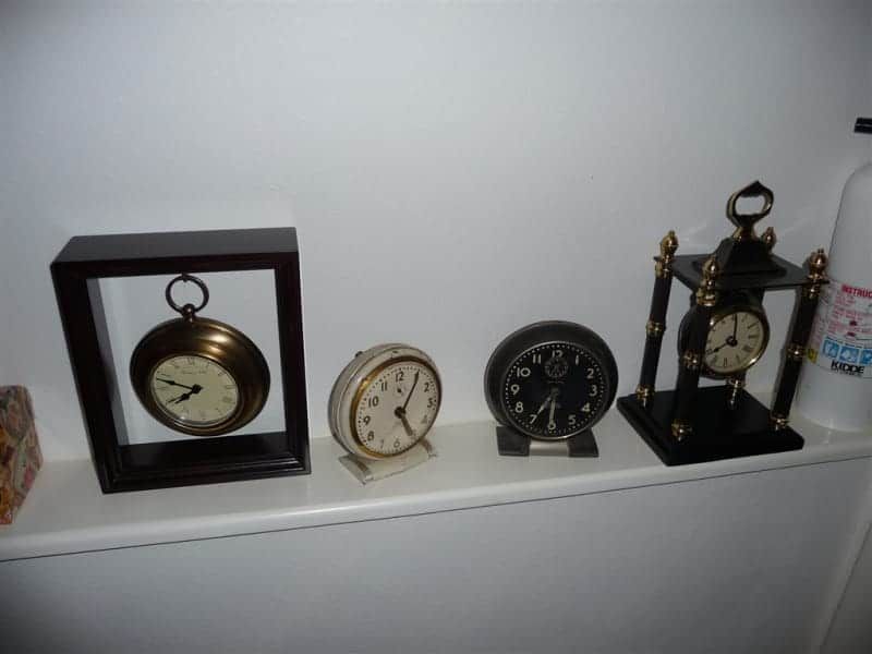 Four clocks on a shelf including a pocket watch and an alarm clock