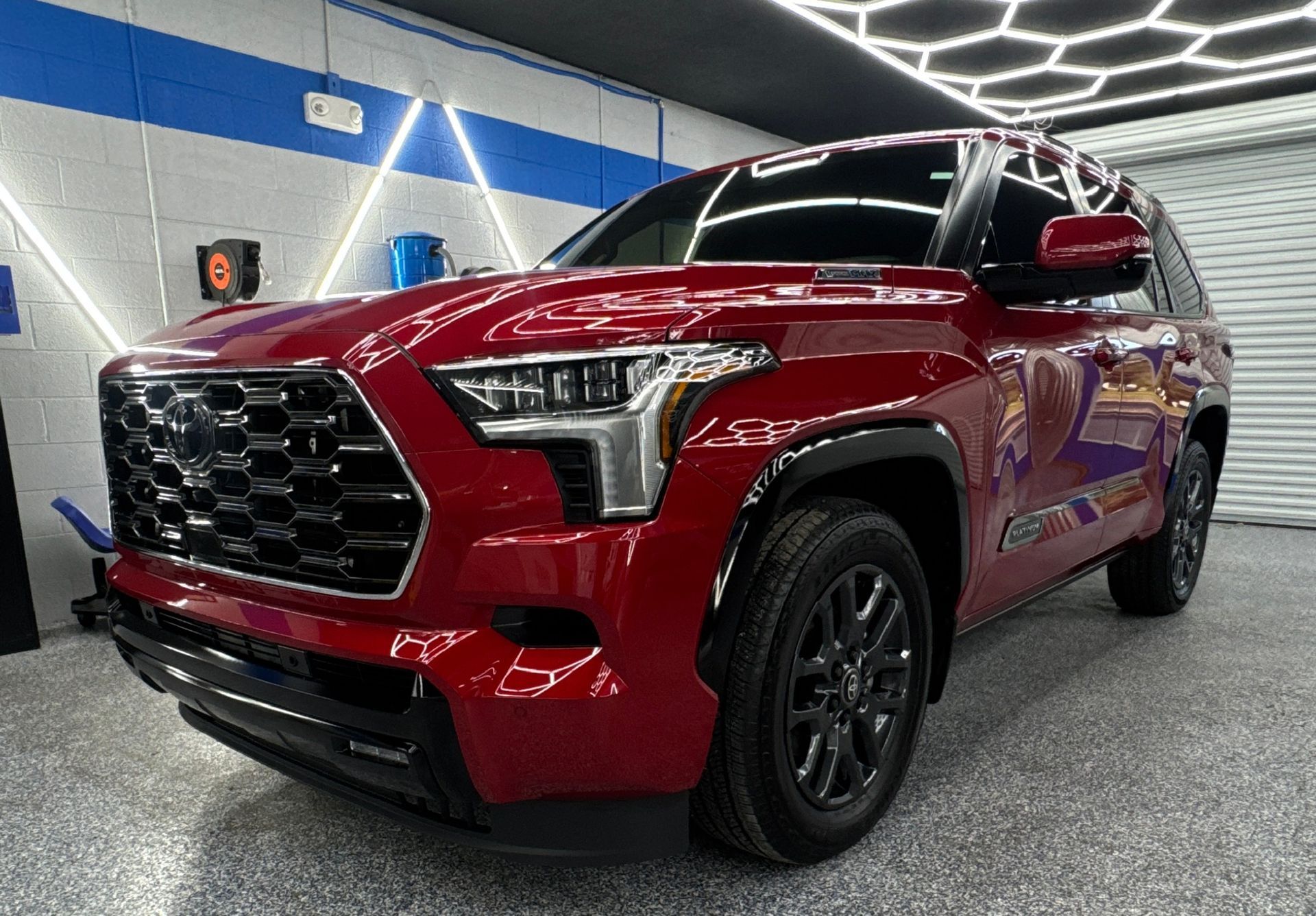 Red SUV in a garage, black wheels, shiny finish, honeycomb grill.