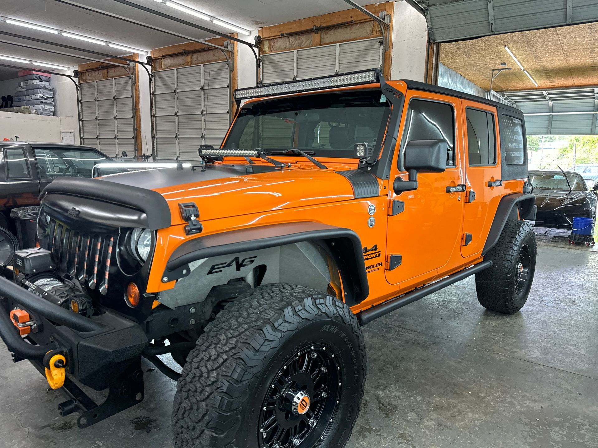 Bright orange Jeep Wrangler with black accents and large tires parked inside a garage.