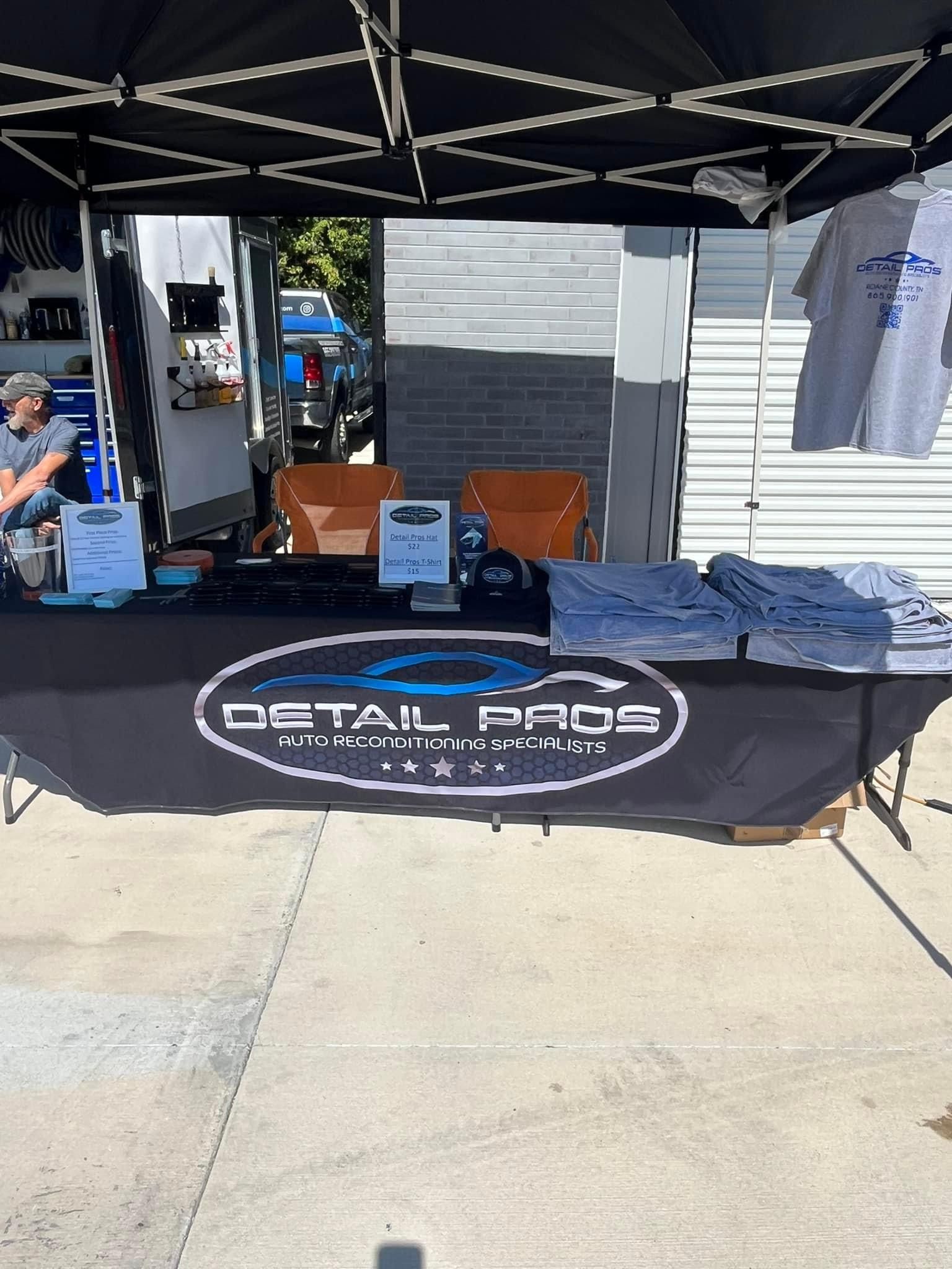 A Detail Pros booth at an outdoor event with products, a table, and branded banner.