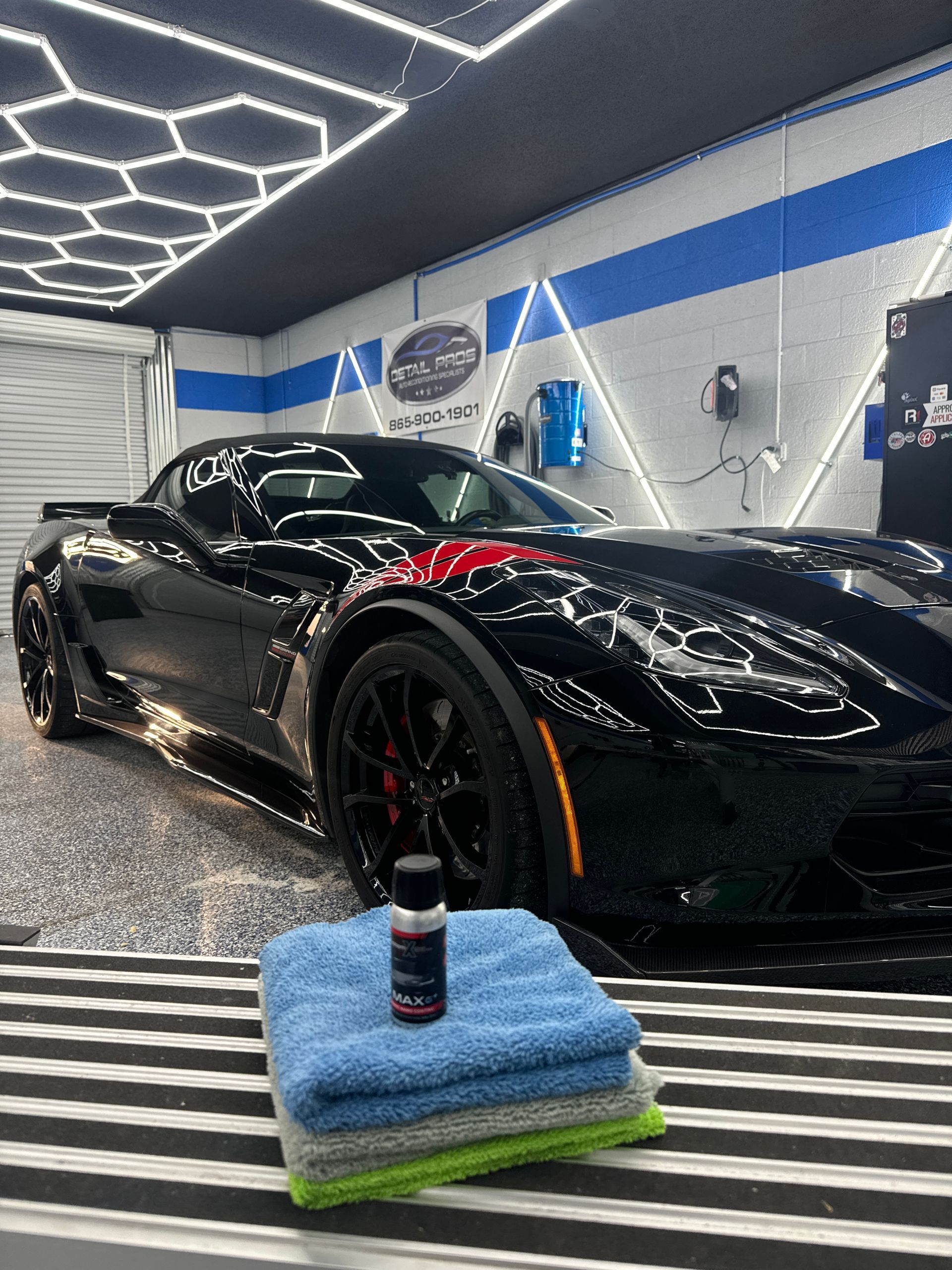 Black Corvette in a detailing shop, with towels and a bottle of car detailing product.