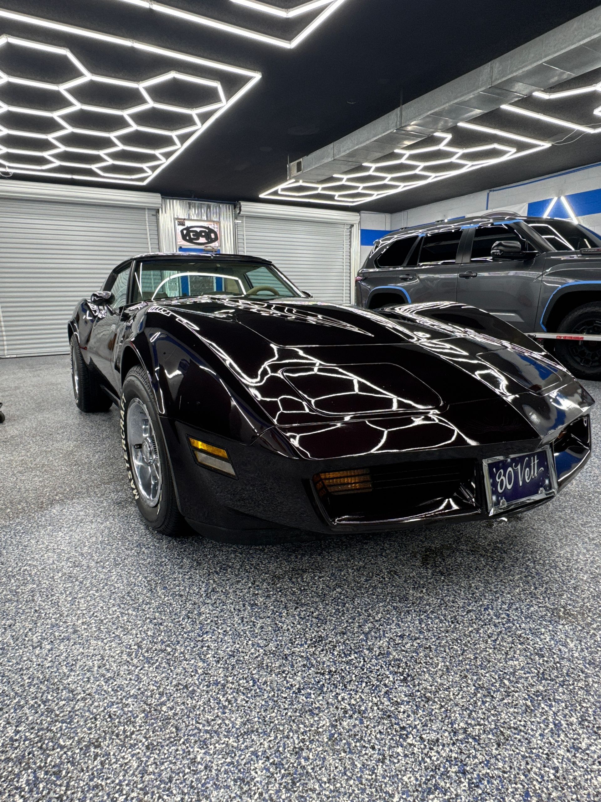 Black classic Corvette sports car in a well-lit garage with a hexagonal ceiling light fixture.