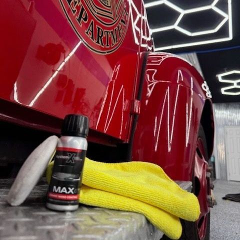 Red car with detailing supplies: applicator, spray, and microfiber cloth.