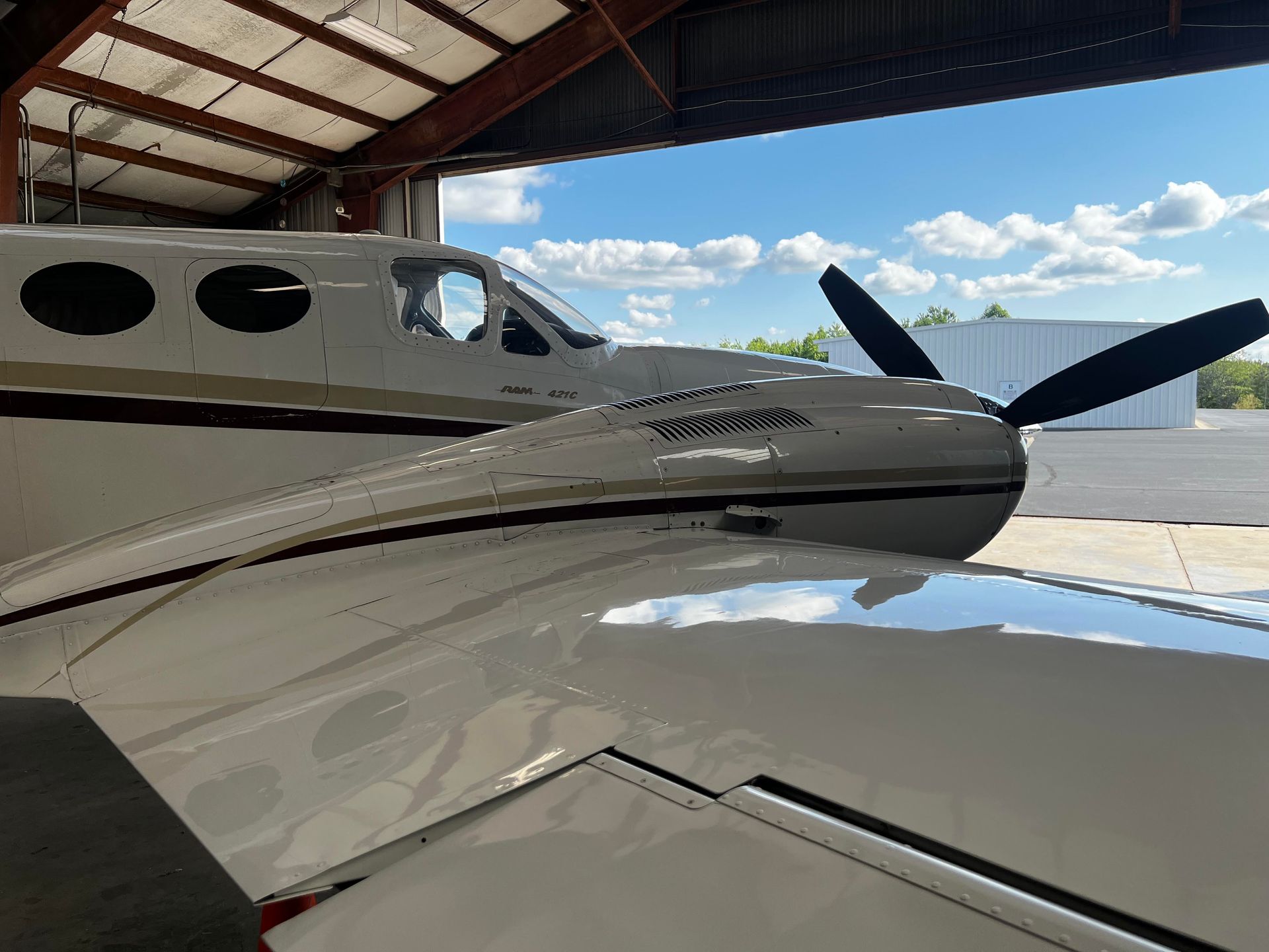 White and gold propeller plane in an open hangar on a sunny day.