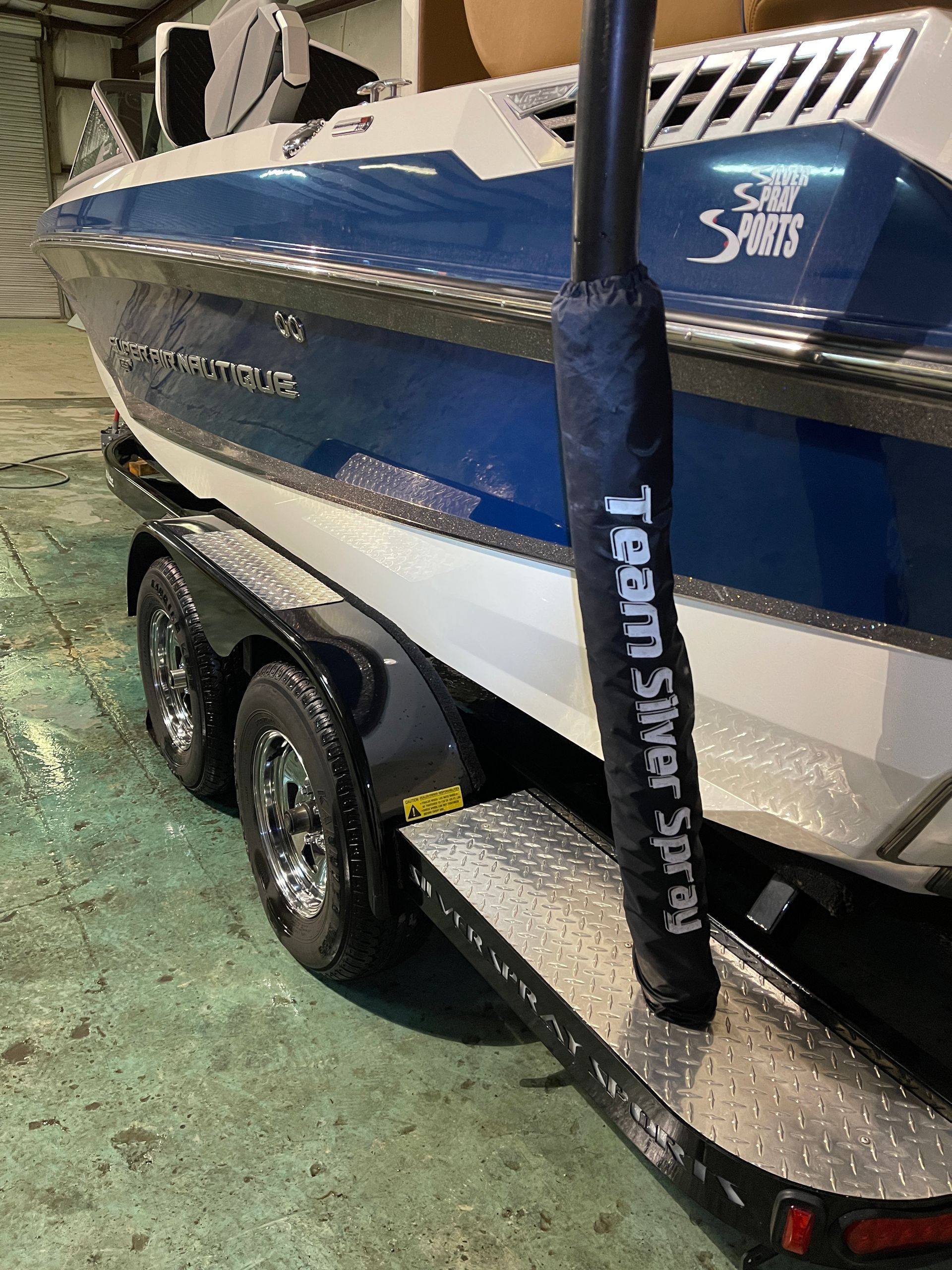A blue and white boat is parked on a trailer in a garage.