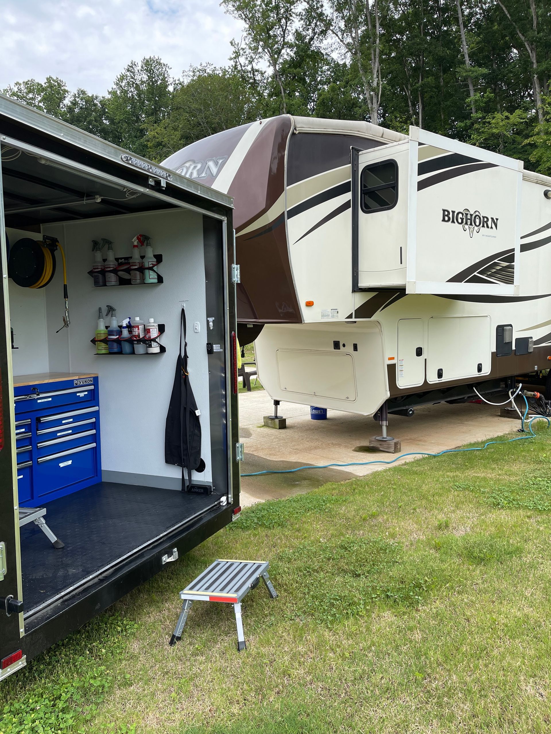 A rv is parked in a grassy field next to a trailer.