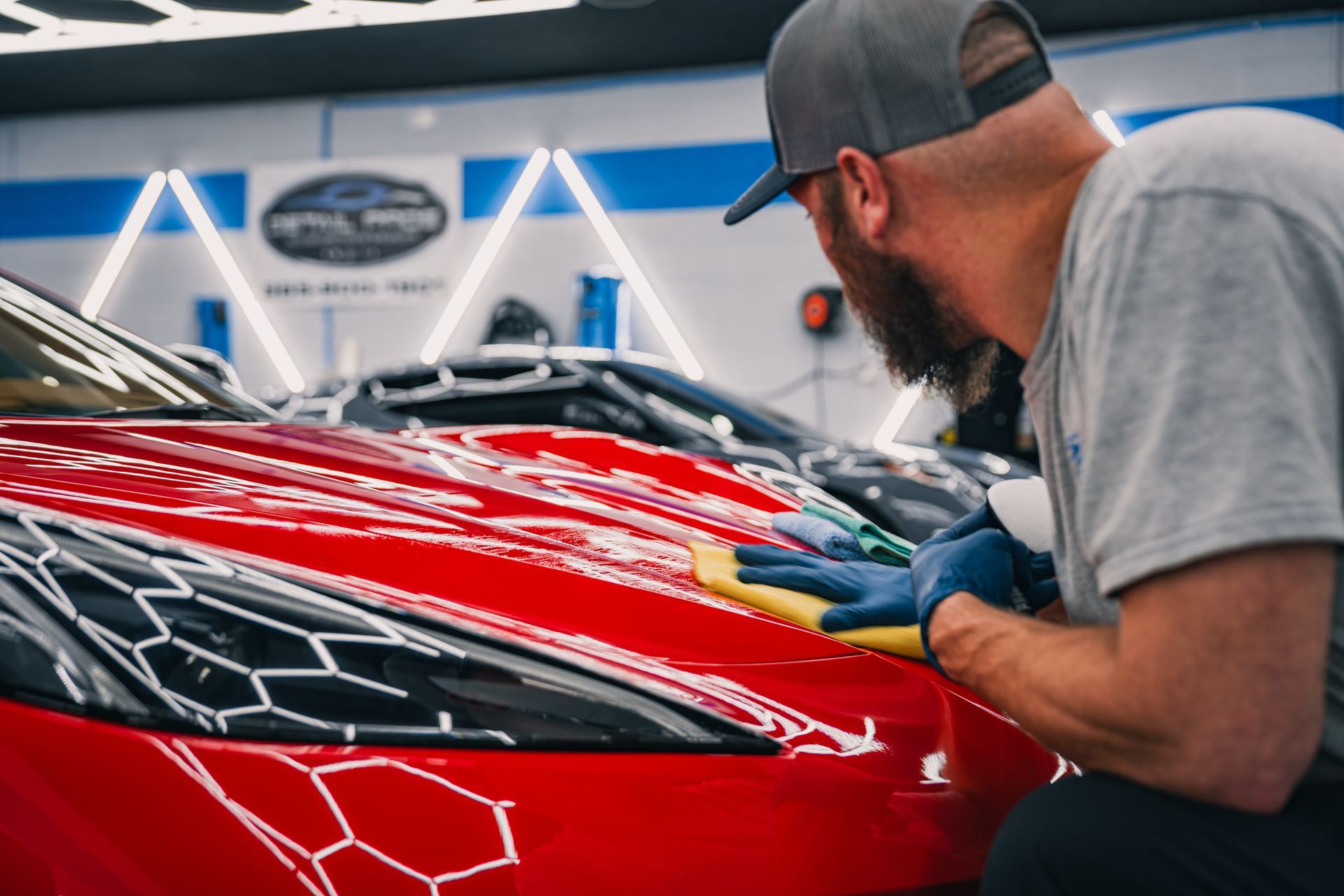 A man is cleaning the hood of a red car in a garage.