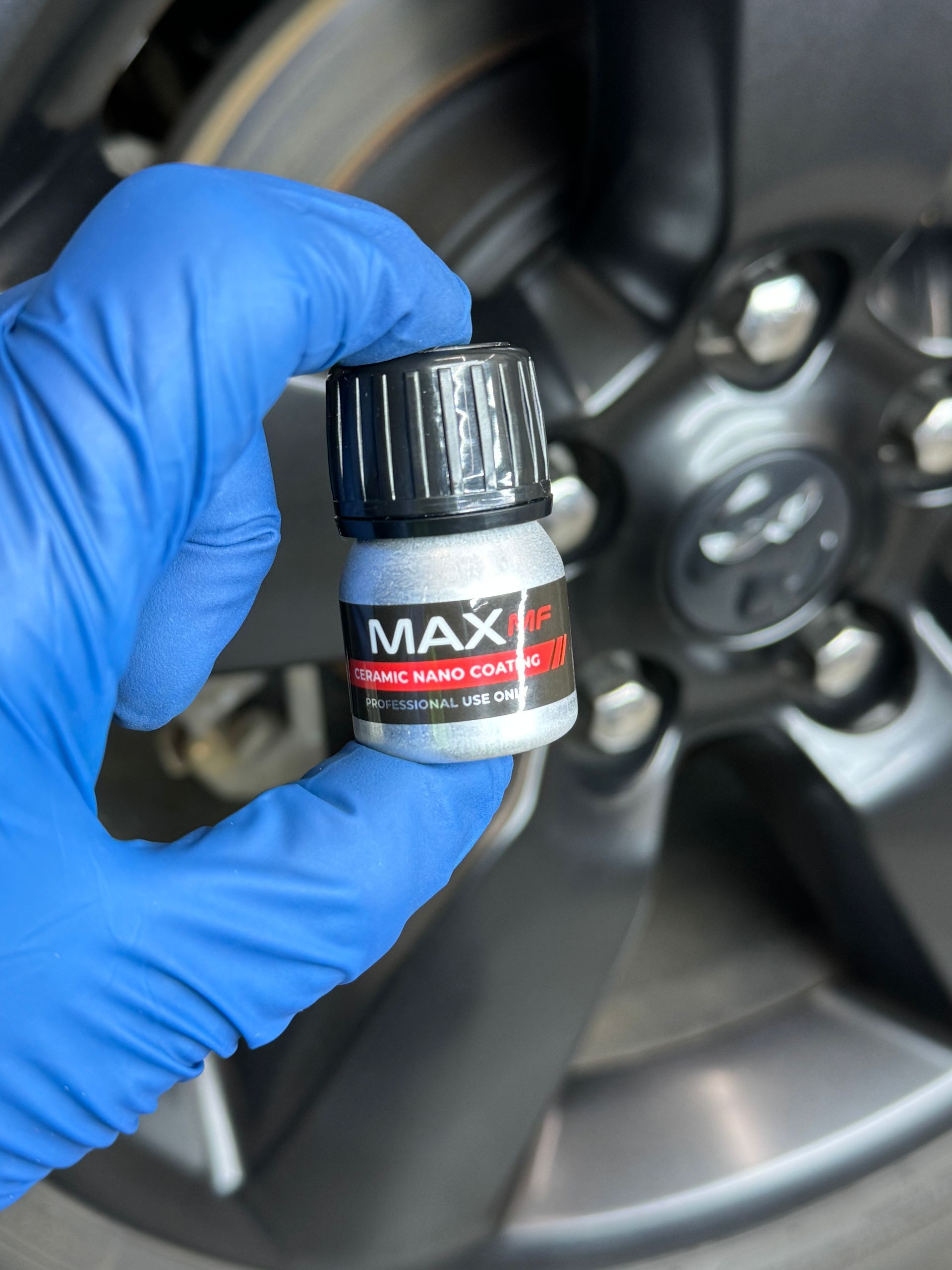 A person wearing blue gloves is holding a bottle of max