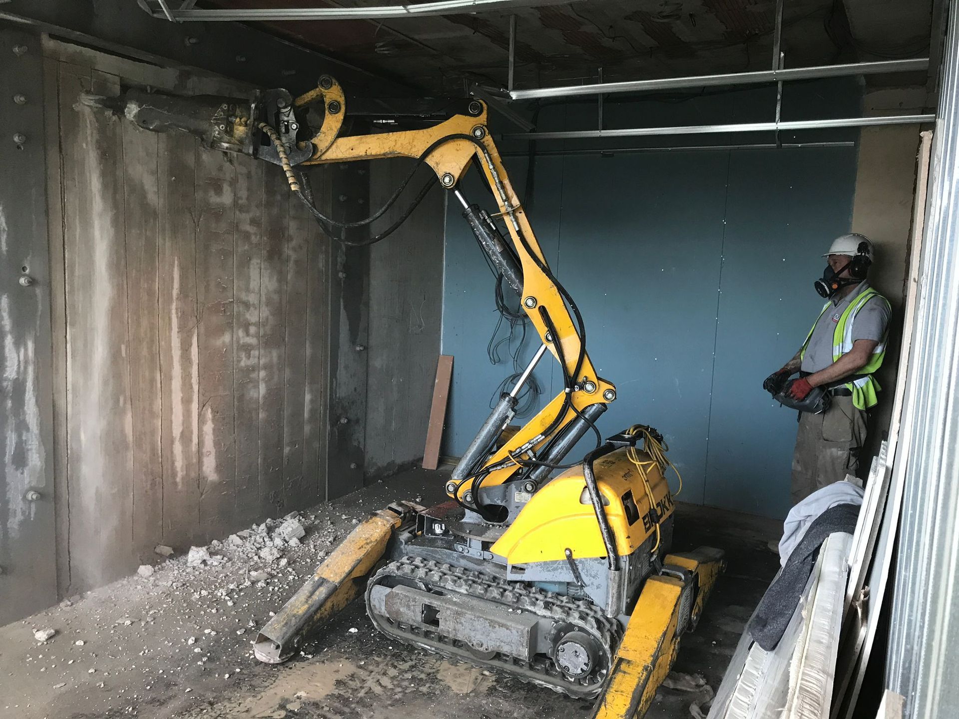 A man is standing next to a yellow excavator in a room.