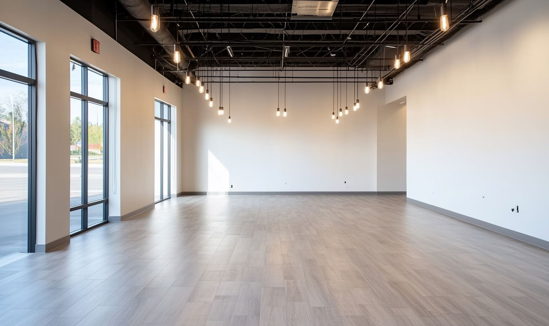 A large empty room with a wooden floor and lots of windows.