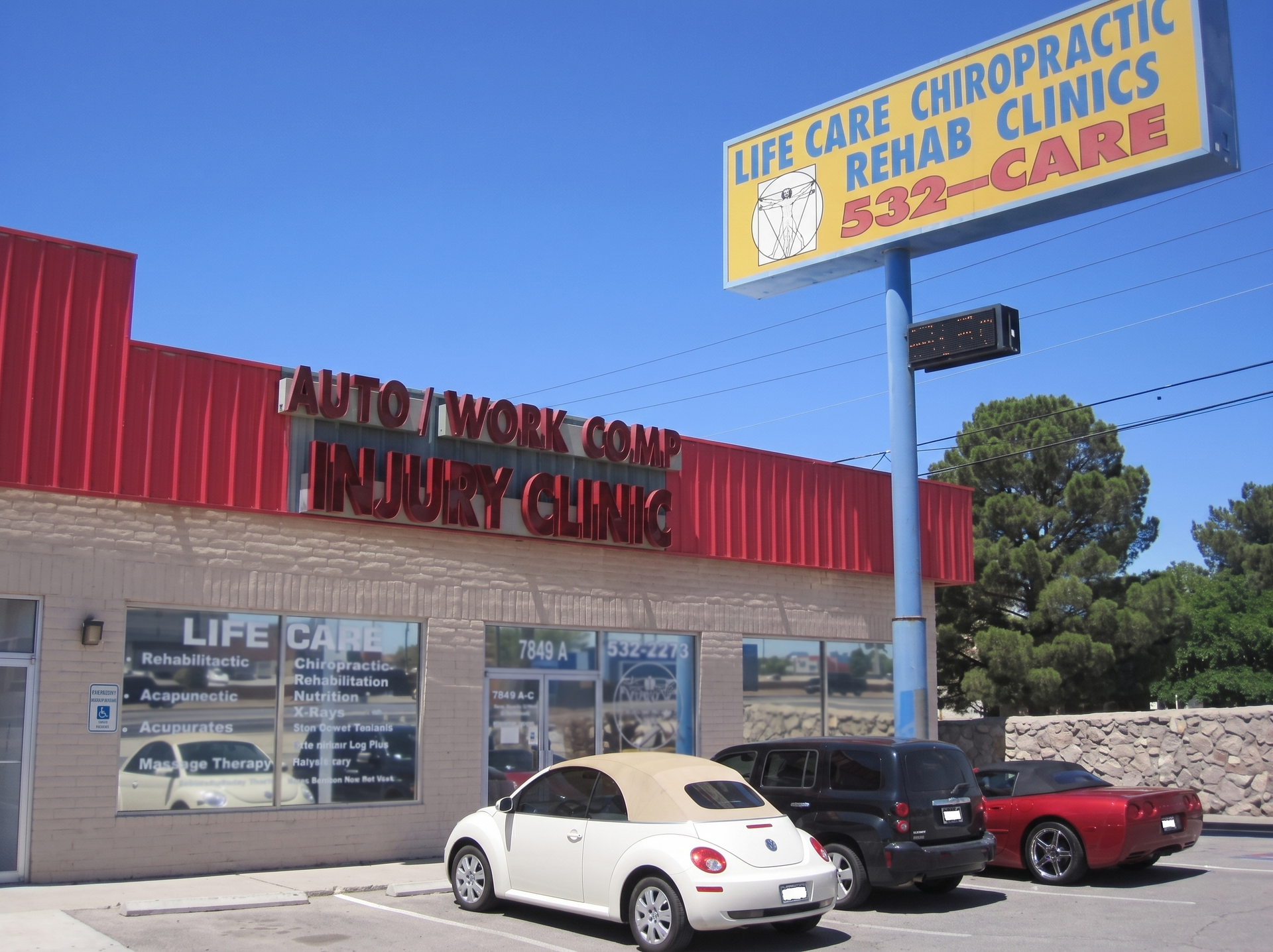 Strip mall storefronts with a chiropractic clinic sign, red awning, and parked cars under a blue sky