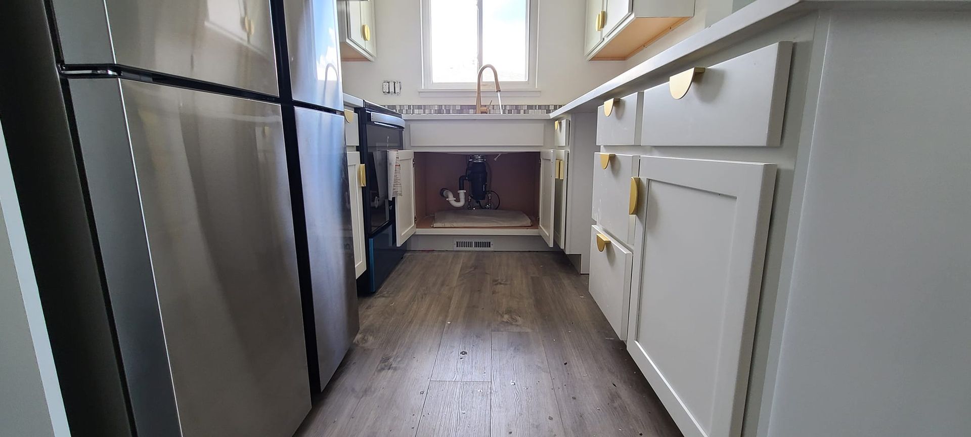 A kitchen with white cabinets, a stainless steel refrigerator, and a window above the sink.