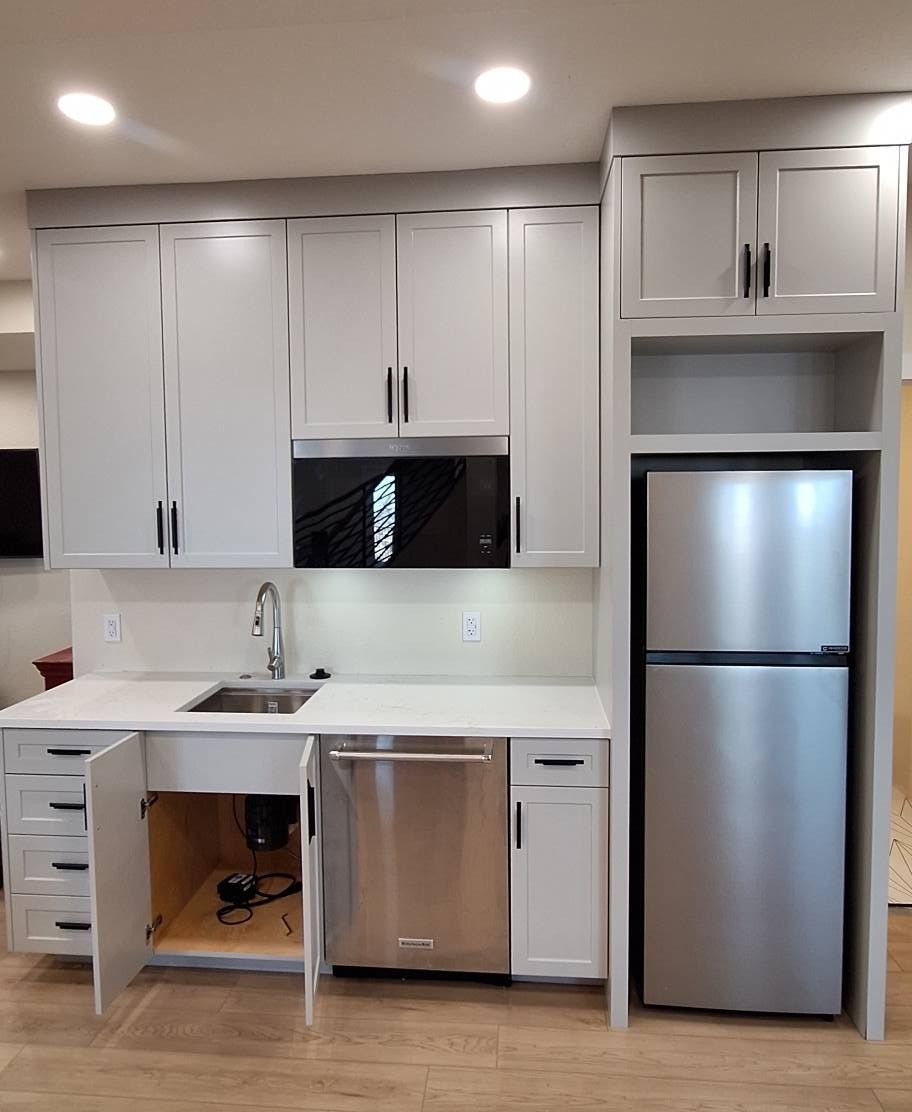 Small white kitchen with a stainless steel refrigerator, microwave, and dishwasher; cabinets and countertops.