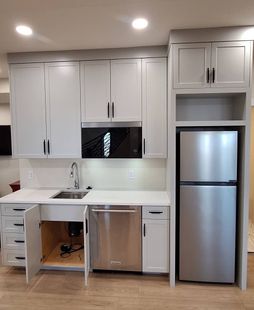 Small white kitchen with cabinets, sink, microwave, and refrigerator. Cabinet door open.