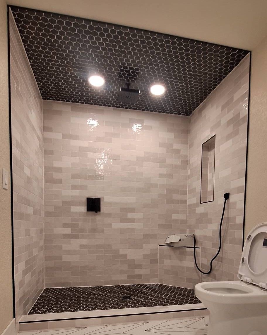 A newly tiled shower with black pebble floor and ceiling, light gray brick-like walls, and two recessed lights.