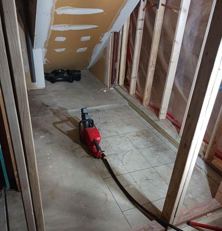 Red demolition saw on floor in a room under construction with wood framing and pipes.
