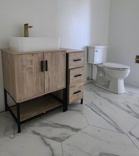 Bathroom with light wood vanity, white sink and toilet, gold faucet, and marble-look floor.