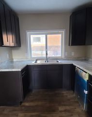 Dark-cabinet kitchen with a window above the sink, light countertops, and an unfished dishwasher.