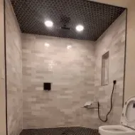 A newly tiled shower with black pebble floor and ceiling, light gray brick-like walls, and two recessed lights.