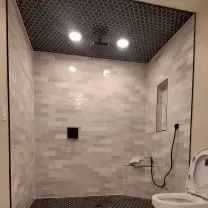 A newly tiled shower with black pebble floor and ceiling, light gray brick-like walls, and two recessed lights.