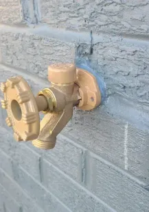 Tan outdoor water faucet on a gray brick wall.