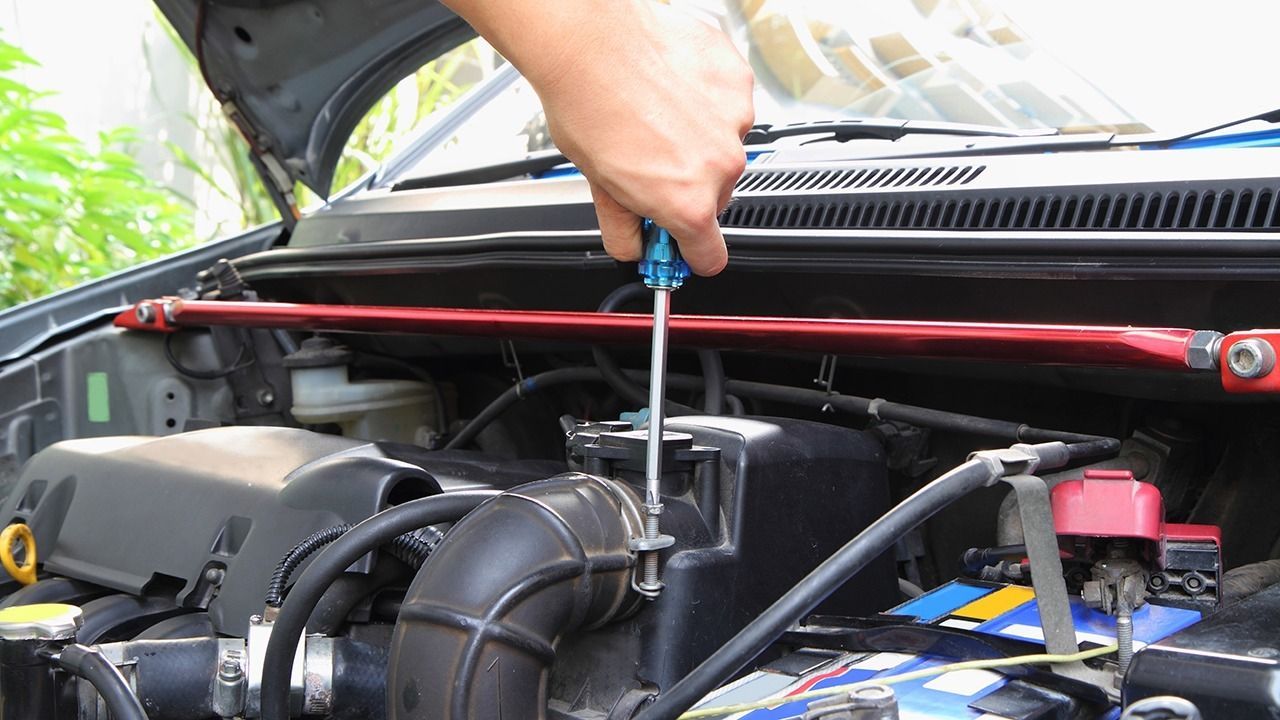 A person is working on the engine of a car with a screwdriver.