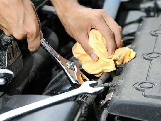 A person is working on a car engine with a wrench and a towel.