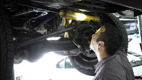 A man is looking under a car with a flashlight.