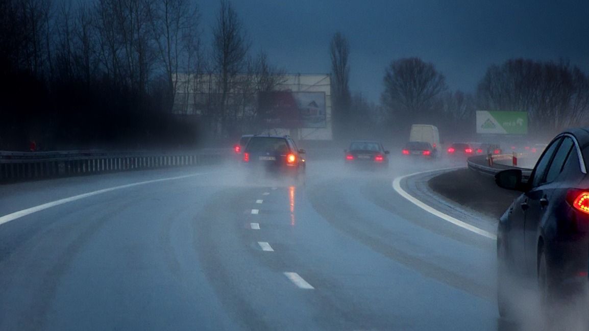 A car is driving down a highway in the rain at night.