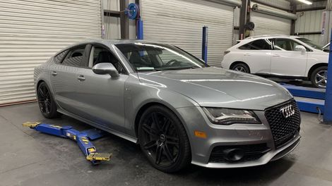 A silver audi a7 is parked on a lift in a garage.