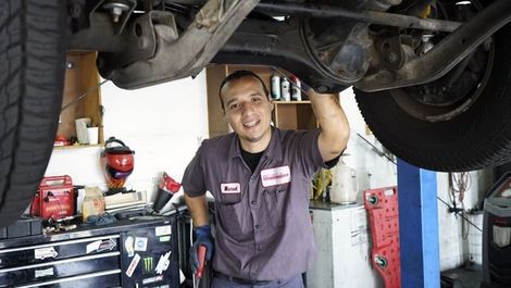 A man is standing under a car in a garage.