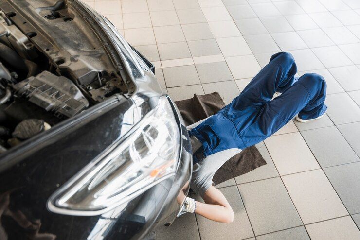 A man is laying on the floor under the hood of a car.