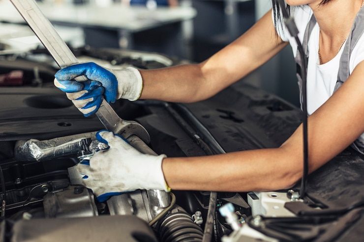 A woman is working on a car engine with a wrench.