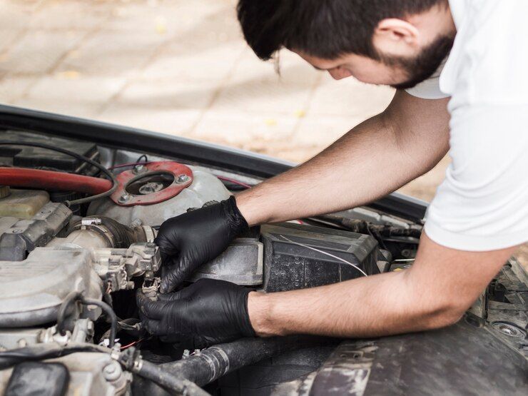 A man wearing black gloves is working on the engine of a car.