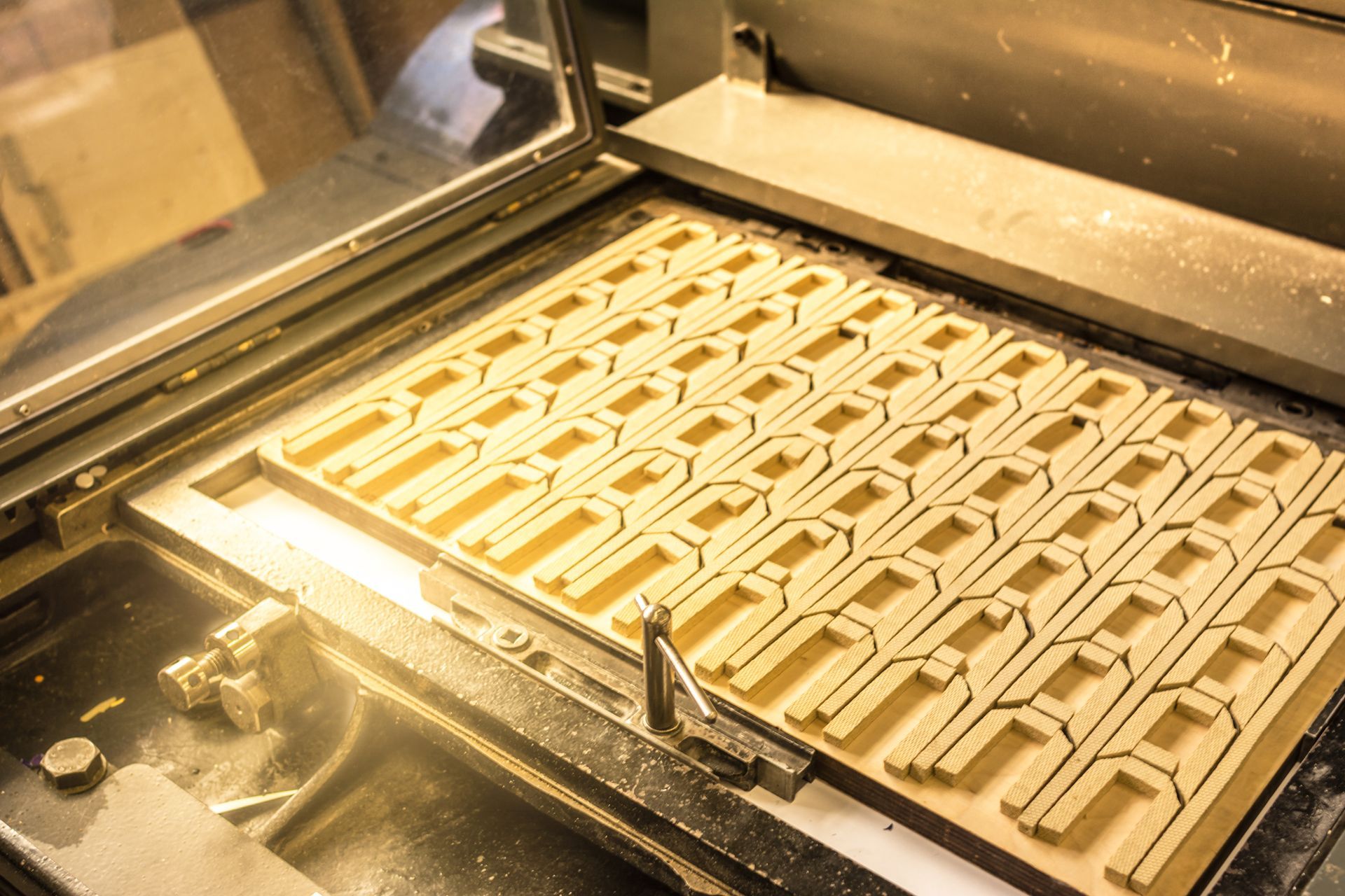 A batch of identical, U-shaped light-tan industrial components arranged in rows on a tray inside a manufacturing machine.