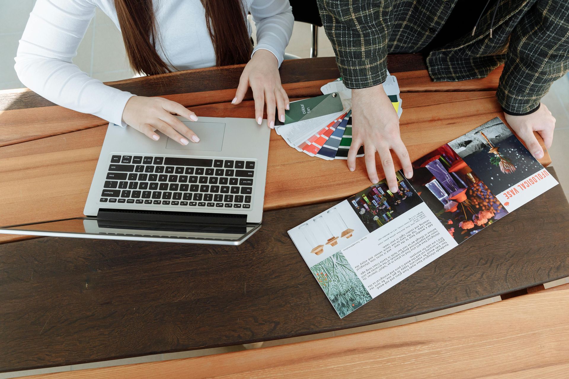 A man and a woman are sitting at a table with a laptop and a magazine.