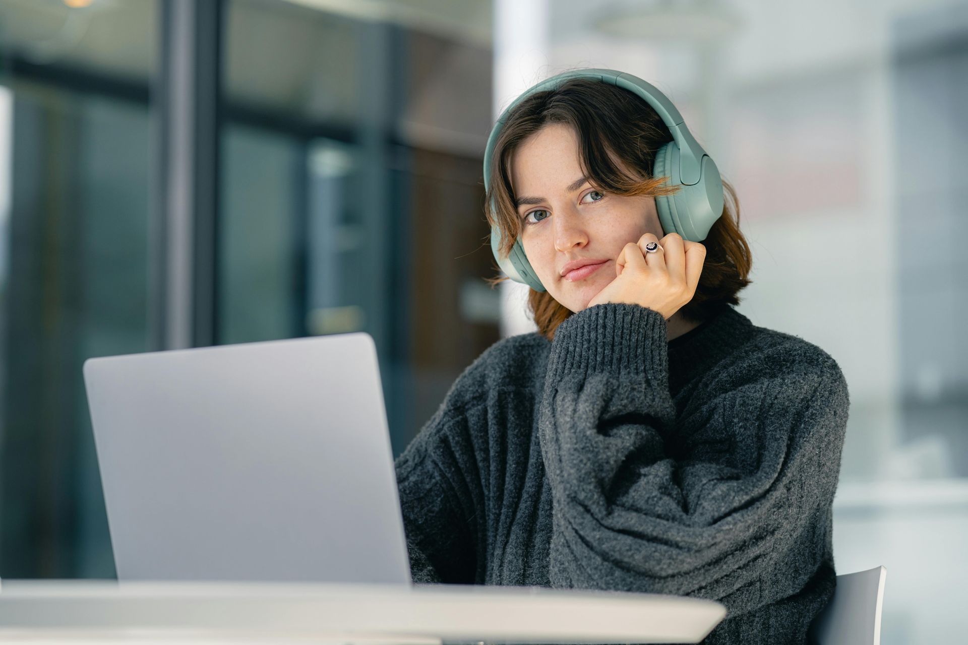 A woman wearing headphones is sitting at a table with a laptop.