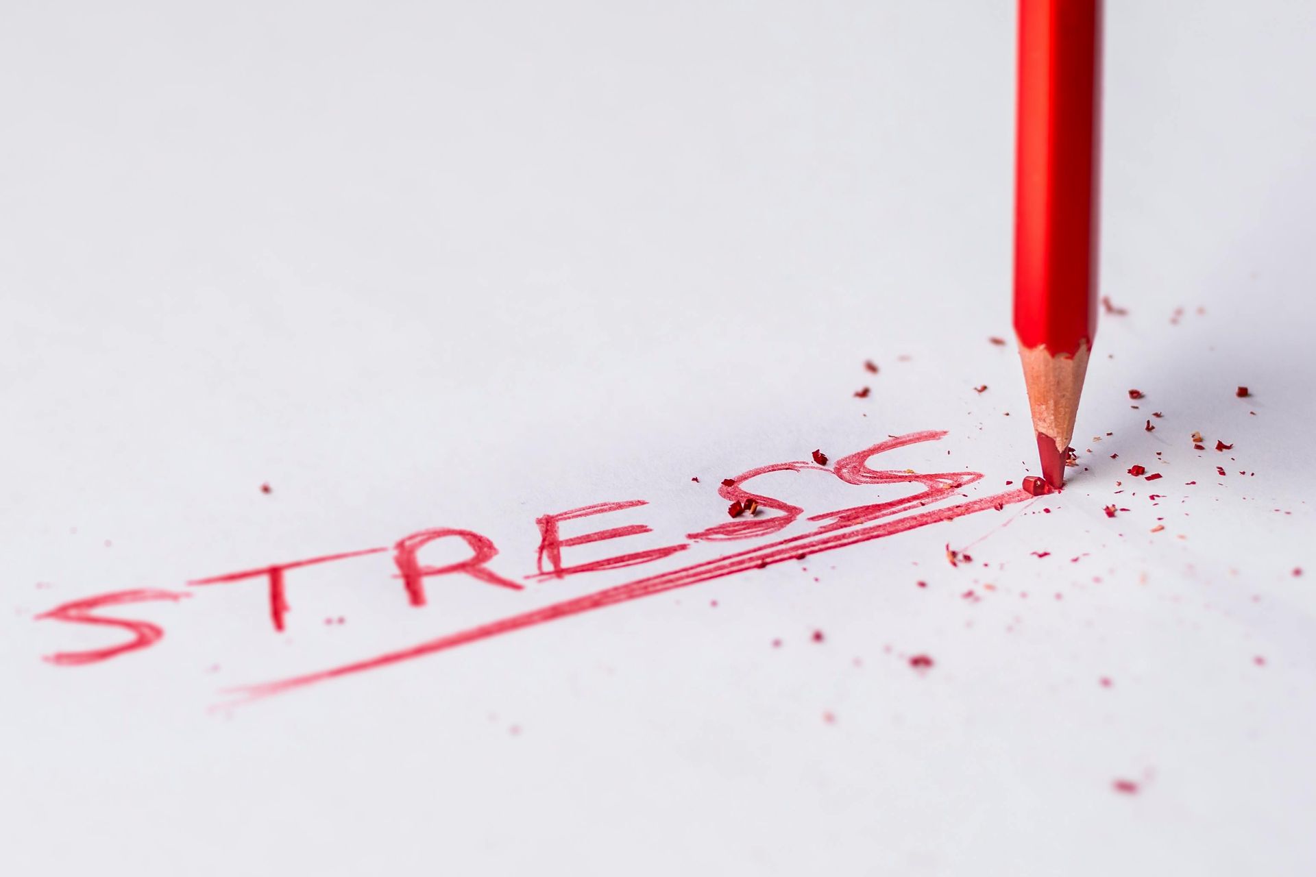 A red pencil is shaving the word stress on a piece of paper.