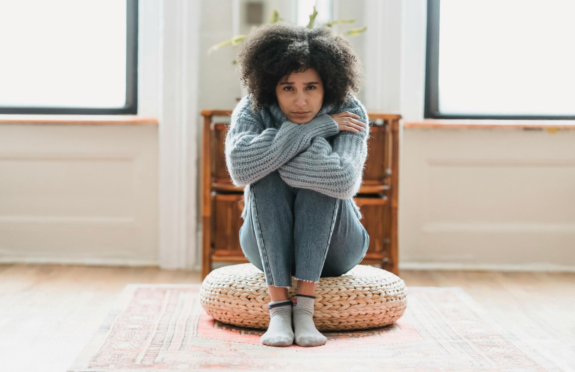 A woman is sitting on a pillow on the floor in a living room.