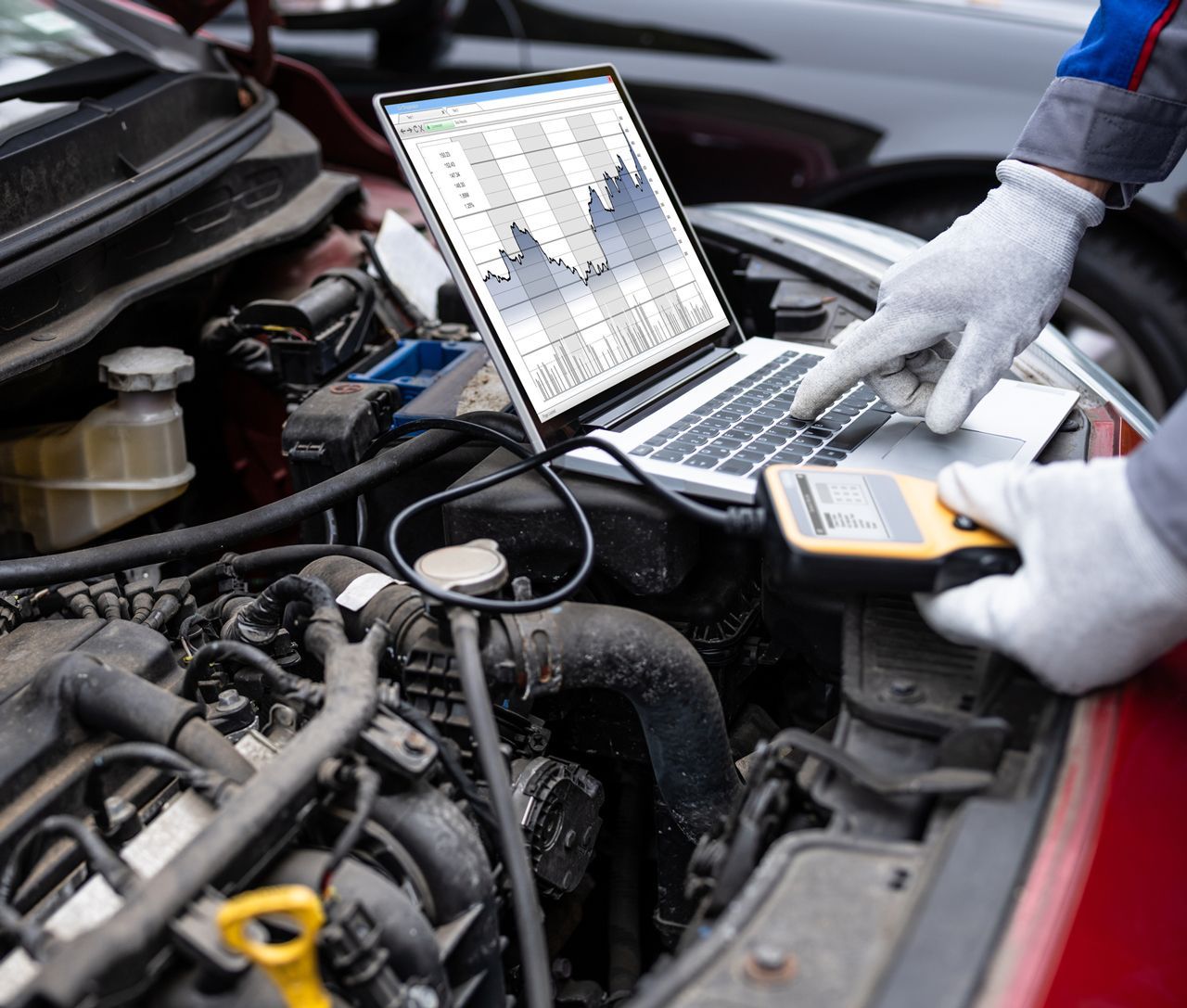 A person is using a laptop computer under the hood of a car