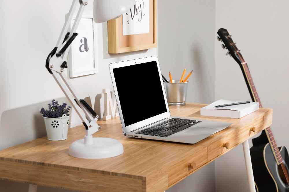 A laptop computer is sitting on a wooden desk next to a guitar.