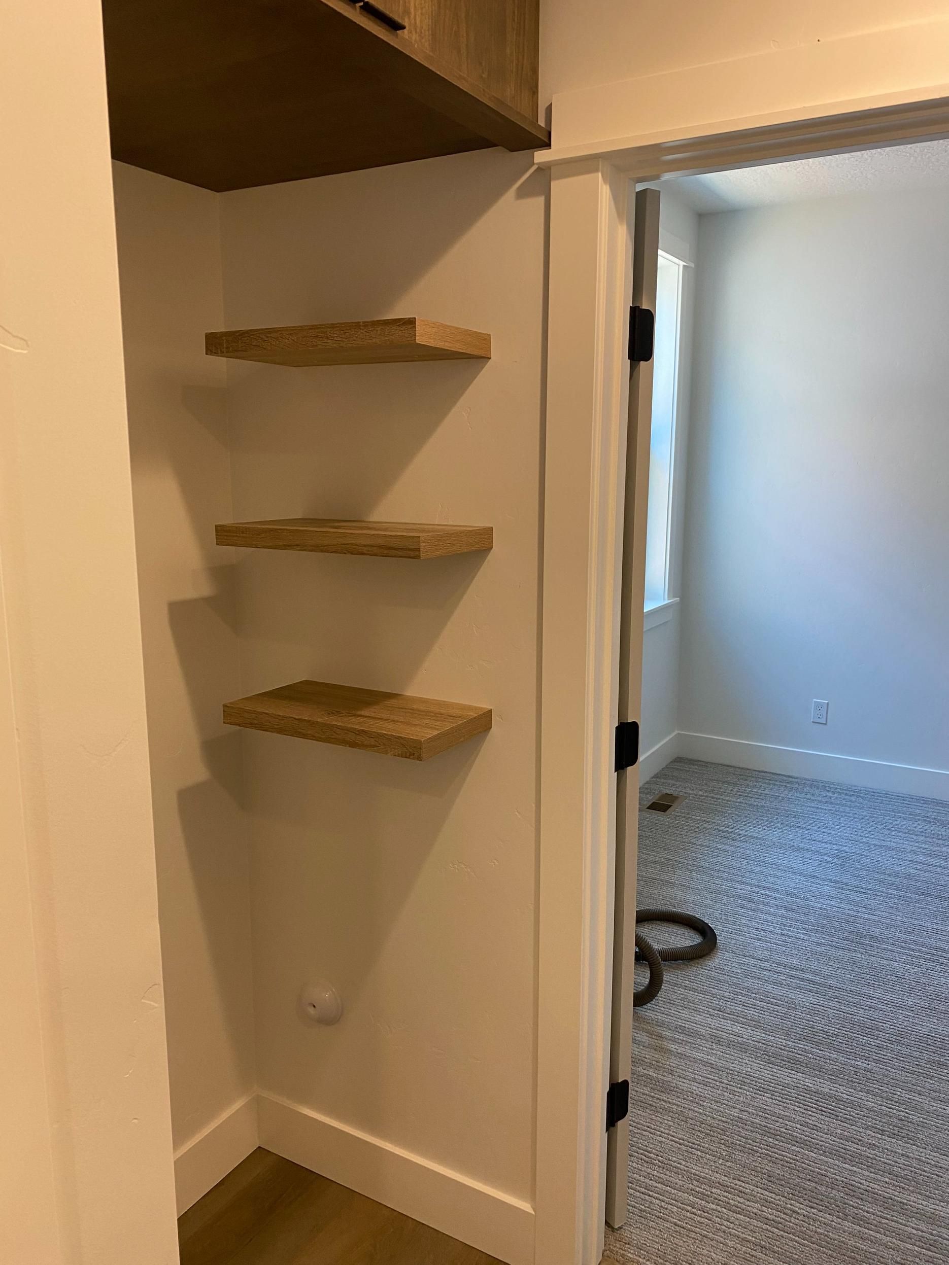 A closet with three shelves and a door leading to a bedroom.