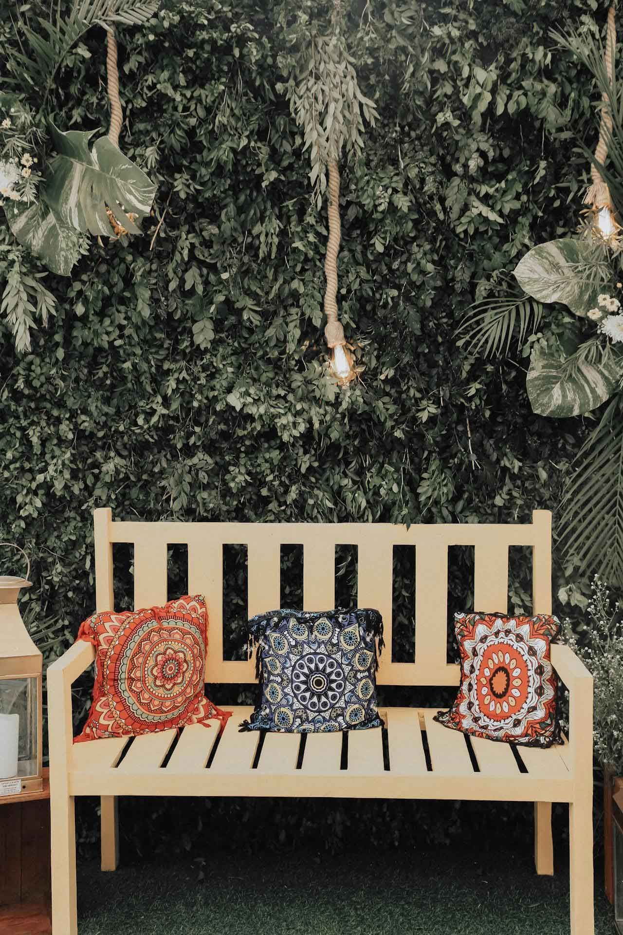 A wooden bench with colorful pillows on it in front of a green wall.