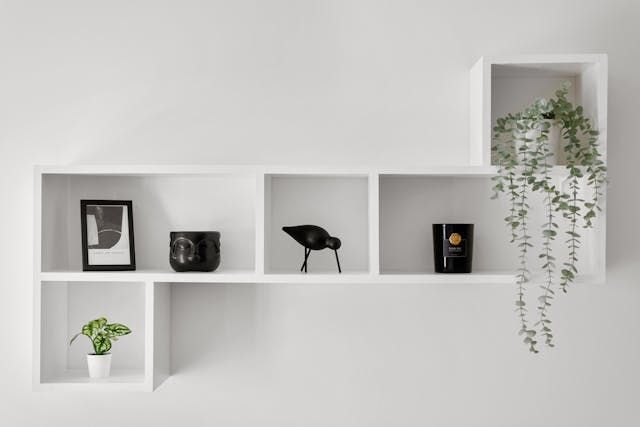 A white shelf with a plant and candles on it.